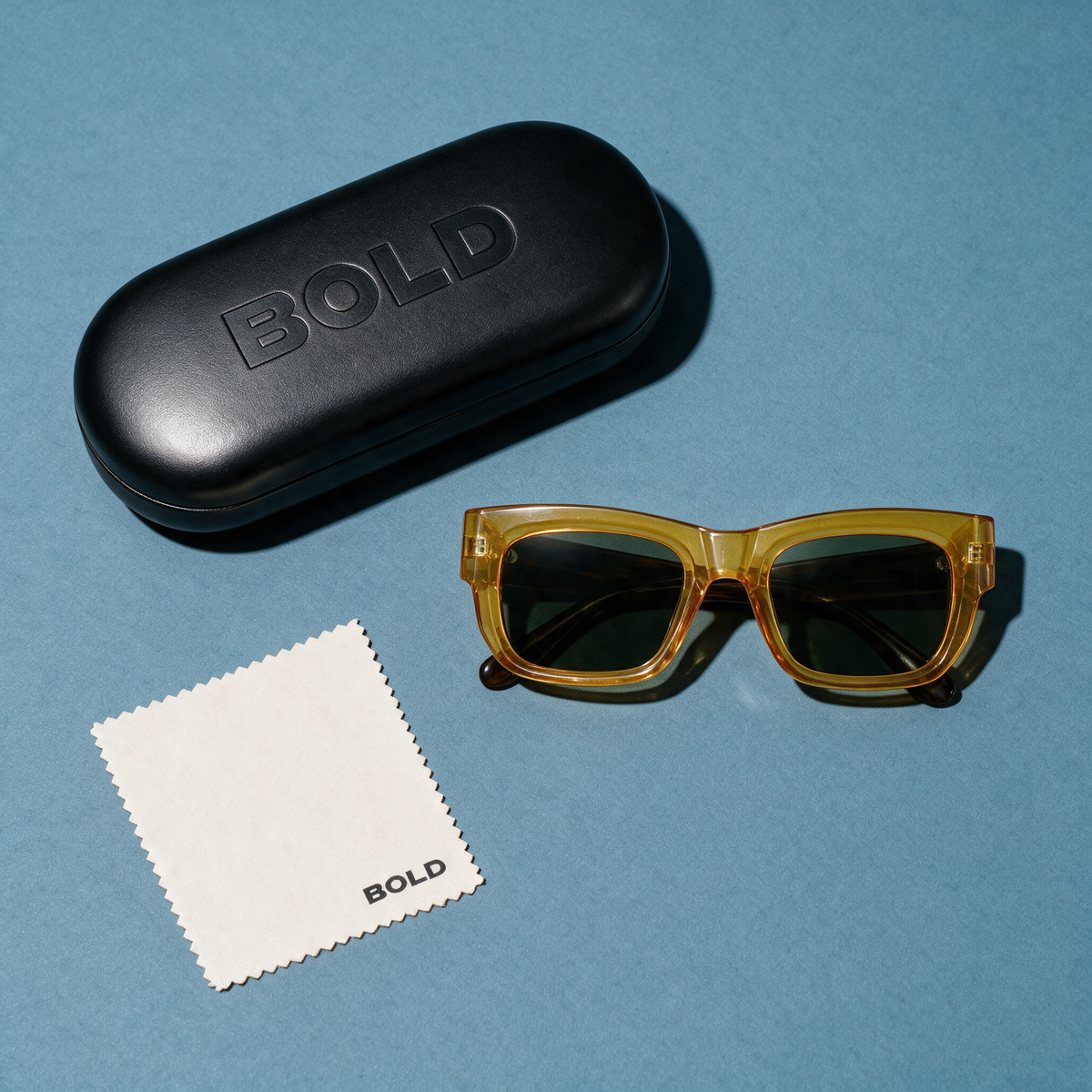 CHISEL Frame 22 sunglasses in SAFFRON, flat lay with BOLD hard case and cleaning cloth